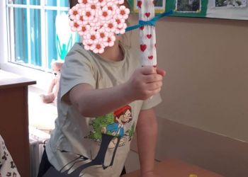 Powiększ zdjęcie: Dziecko z zasłoniętą twarzą trzymające kukiełkę