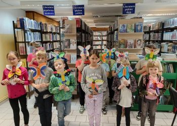 Powiększ zdjęcie: Zdjęcie grupowe dzieci w bibliotece. Dzieci trzymają w dłoniach motyle
