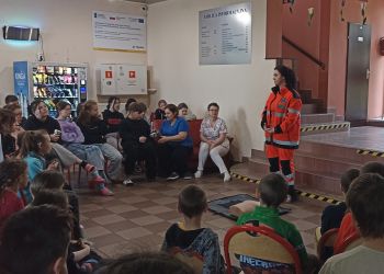 Powiększ zdjęcie: dzieci i dorośli siedzący na korytarzu