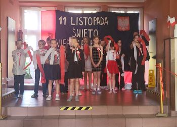 Powiększ zdjęcie: dzieci na scenie - z tyłu dekoracja z napisem 11 Listopada Święto Niepodległości