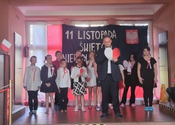 Powiększ zdjęcie: uczniowie na scenie, z tyłu dekoracja z napisem 11 Listopada Święto Niepodległości