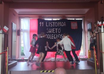 Powiększ zdjęcie: uczniowie tanczą - z tyłu dekoracja z napisem 11 Listopada Święto Niepodległości